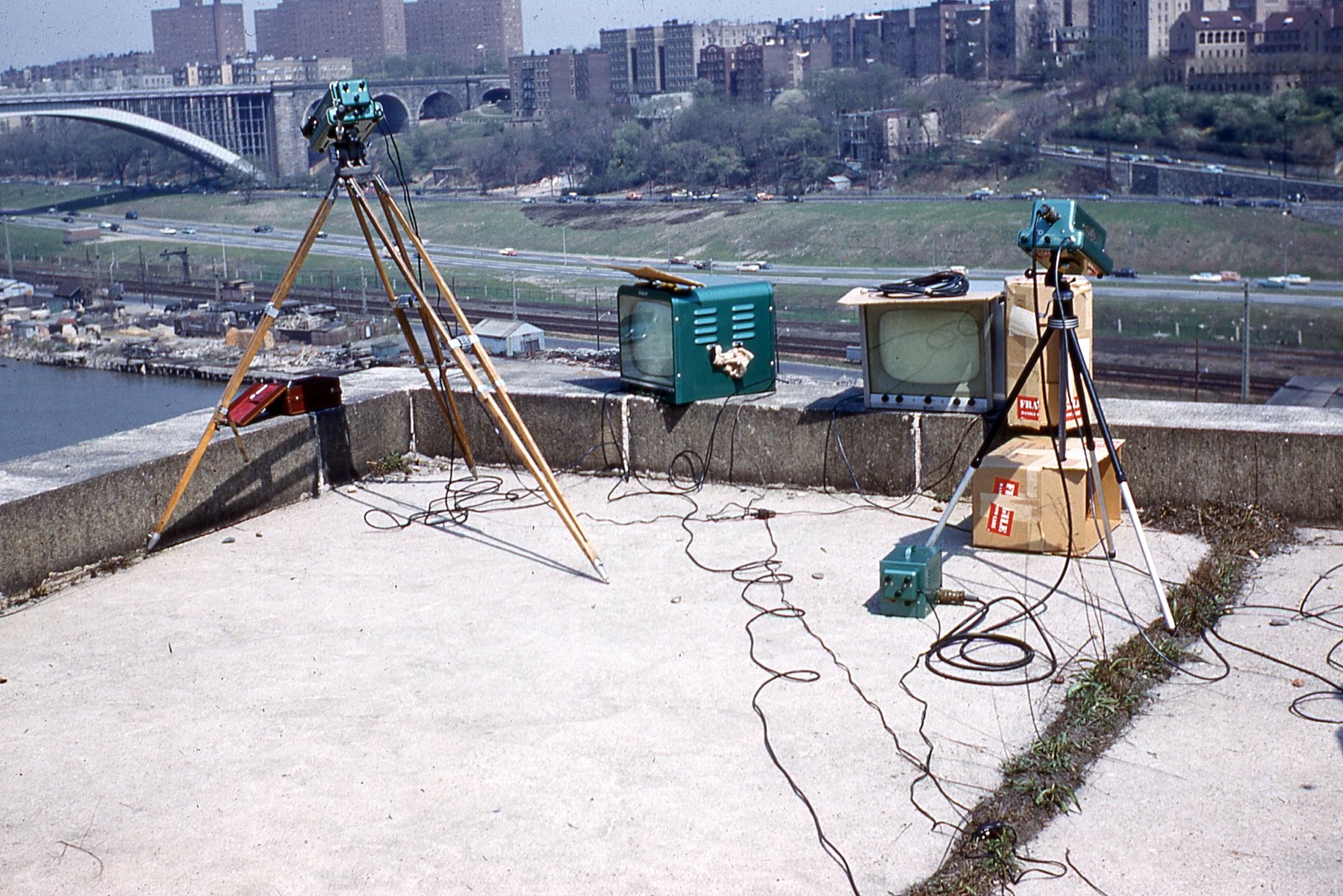Camera equipment on the High Bridge Water Tower overlooking the Harlem River (photo: Bob Norin, W7YAQ) Photo of TV cameras on tripods, monitors, etc. on rooftop overlooking a river and distant buildings