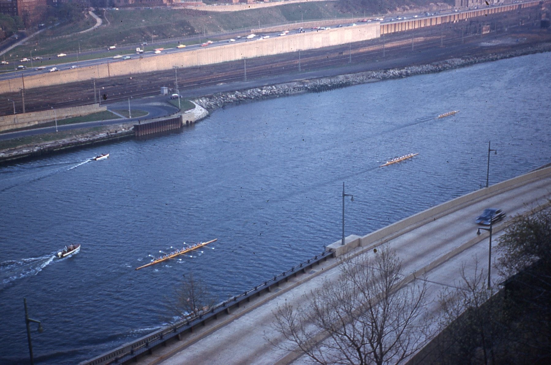 photo looking down from height at 3 distant crew shells and 2 following motorboats.